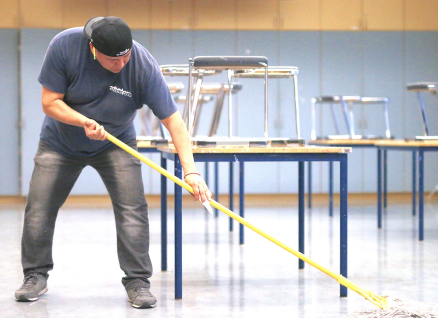 Janitor Rigoberto Perez mops the  floor in an art room after school.